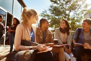 Image: A diverse group of college students engaging in conversation and laughter on a campus lawn, showcasing the joy and camaraderie of making friends at college in the United States. The image is associated with the blog post 'How to Make Friends at College in the US - By Esposearch.